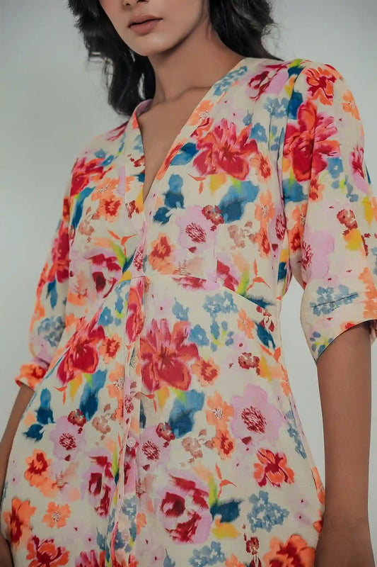 Close-up front view of a model wearing the Tea & Dove Celestial Bloom short linen dress, highlighting the vibrant red, orange, and blue floral pattern, deep V-neckline, and empire waist seam detailing.