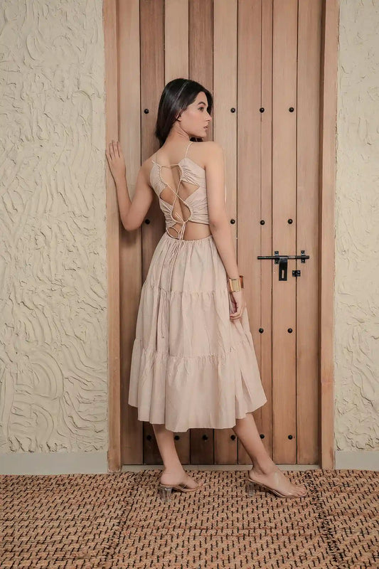 A striking back view of a model showcasing the Tea & Dove Glam Mushroom cotton-lycra dress. Highlights a bold, strappy backless cutout design with criss-cross lace-up detailing and a voluminous tiered midi skirt.