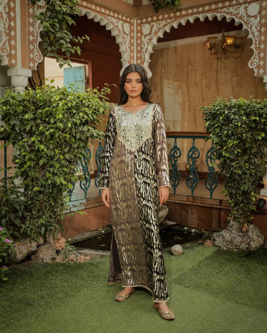 Full-length shot of a woman modeling a long, flowing metallic brown and black printed lurex kaftan with a dramatic mirror-work yoke in an outdoor courtyard.